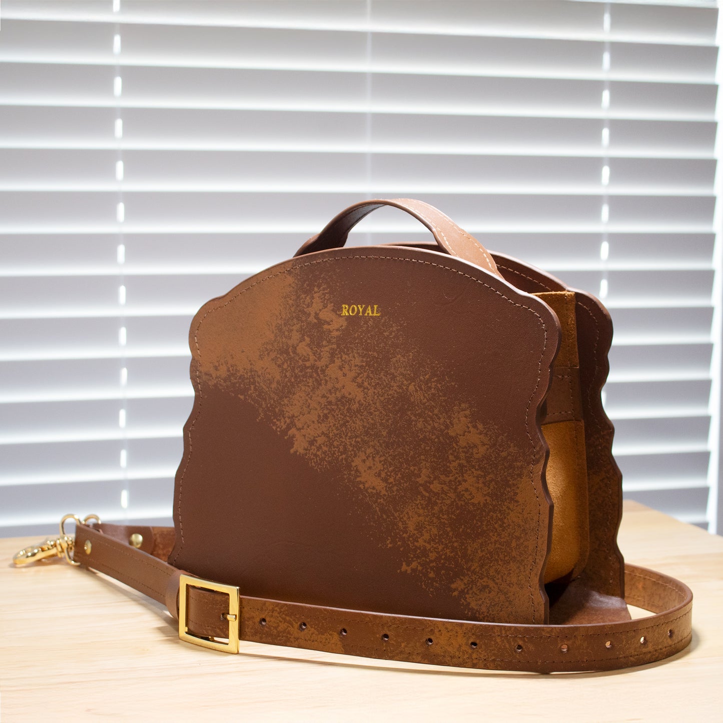 Hand‑painted full‑grain leather Joy satchel handcrafted in brown with artisan multi‑tone accents, shown on a light wooden surface with gold‑tone hardware.