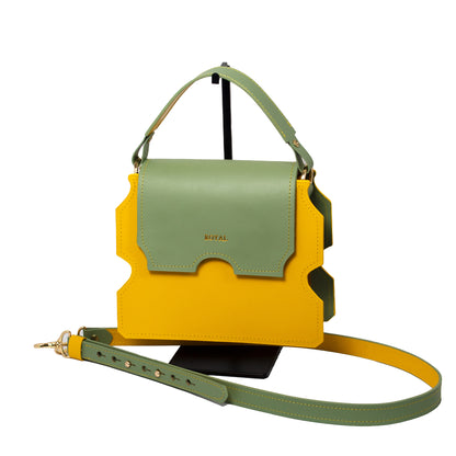 Hand-painted full-grain leather Faith shoulder bag handcrafted in yellow with a pastel mint green flap, shown in a front view with its top handle and custom two-tone strap.  