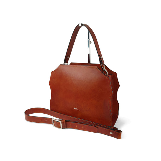 Hand‑painted full‑grain leather Forgiveness structured satchel handcrafted in cognac, shown in a side view on a stand with its removable strap.  