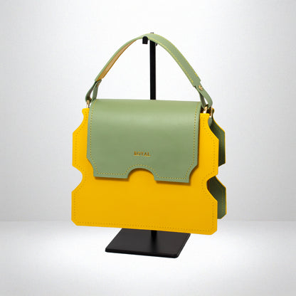 Hand-painted full-grain leather Faith shoulder bag bespoke in yellow with a pastel mint green flap, shown in a slanted side view on a stand.  